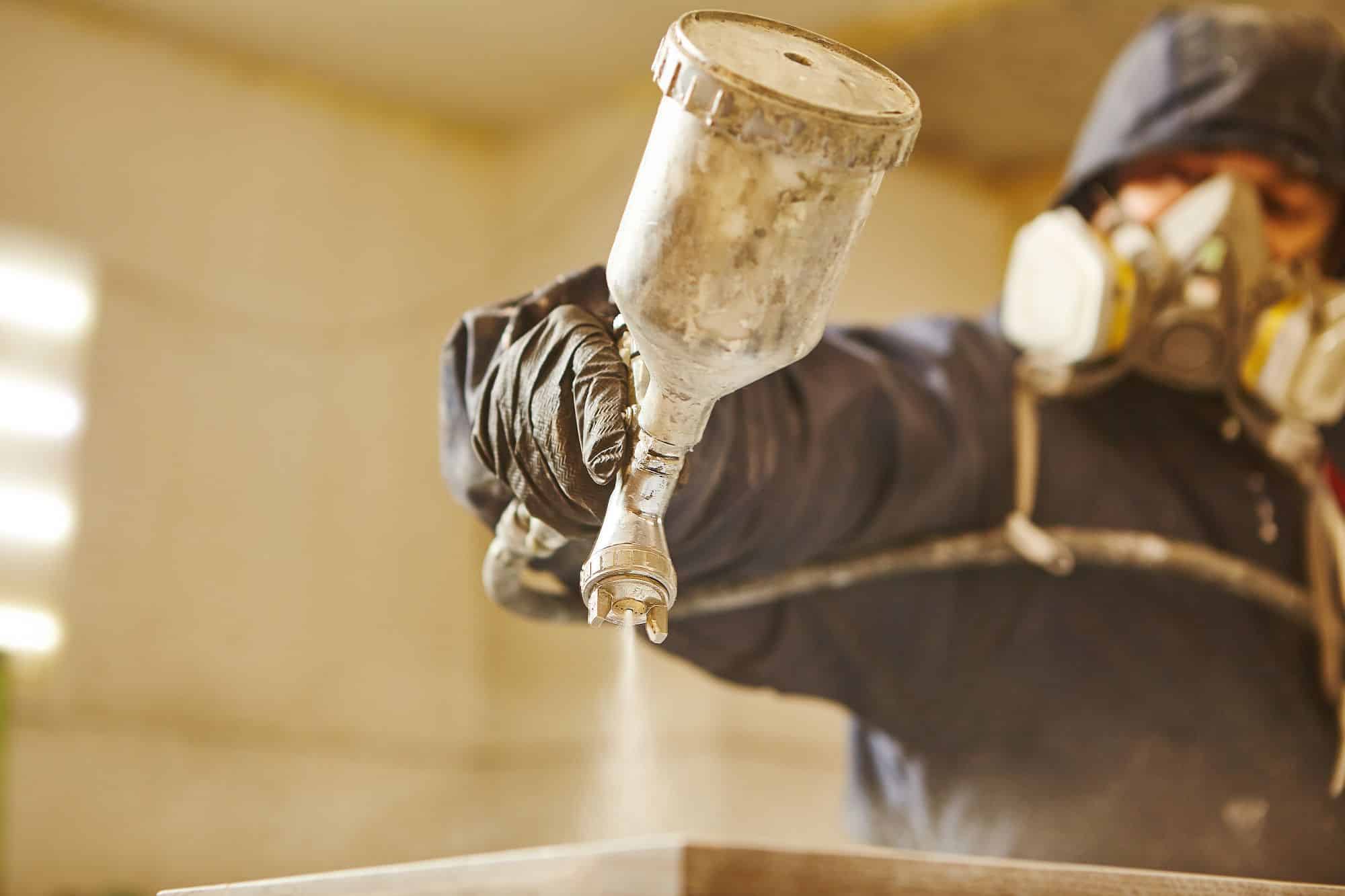 Manual Air Spray Wood Coating Painter in a respirator using a spray gun