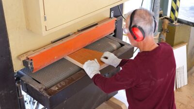prep_wide-belt-sander Operator wearing earmuffs and gloves at a wide belt sander